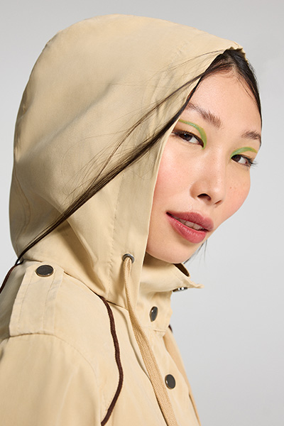 Modelo asiática usa delineador gráfico verde e veste parka bege com capuz, que está sobre a cabeça dela