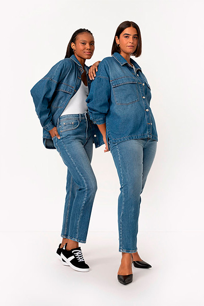 À esquerda, modelo veste jaqueta jeans oversized com regata branca por baixo, calça mom jeans e tênis preto. À direita, outra modelo veste o mesmo look, só que com a jaqueta fechada e sapato preto de bico fino