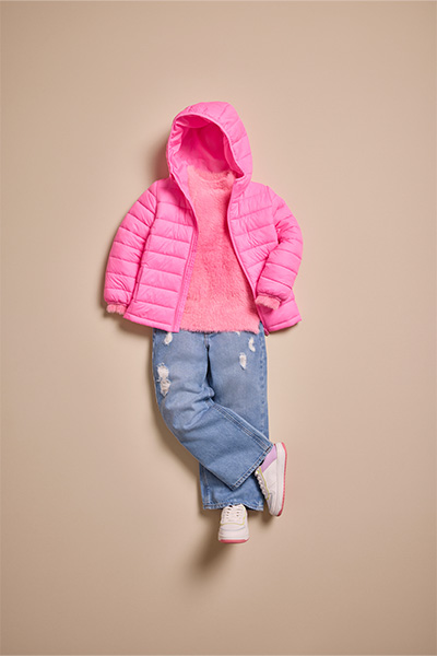Peças infantis fotografadas de cima e montadas como se estivessem vestindo uma criança. Jaqueta puffer rosa, calça jeans e tênis branco.