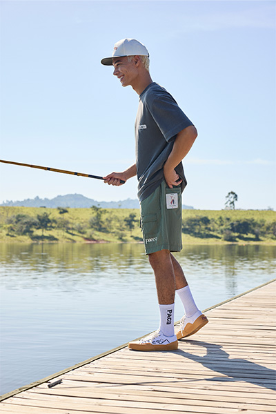 Modelo veste boné branco com aba verde escura, camiseta verde e bermuda verde no mesmo tom, e tênis brancos.
