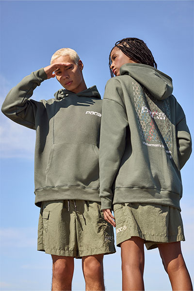 Dois modelos, um homem e uma mulher, vestem as peças da collab C&A e PACE: moletom verde militar com escritos em branco e bermuda verde militar no mesmo tom.