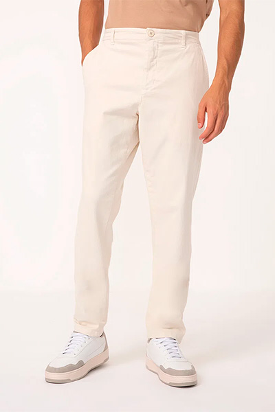Modelo é mostrado apenas da cintura para baixo e veste calça reta branca com tênis branco