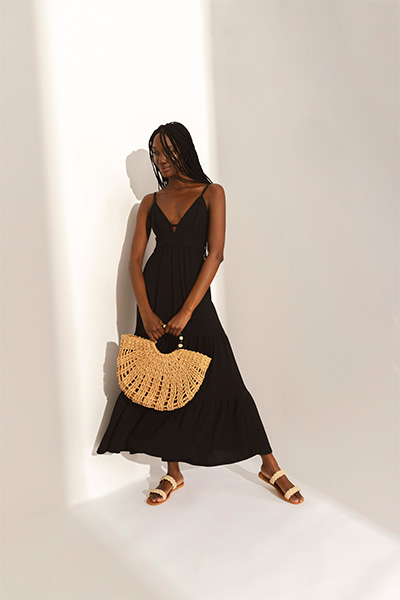 Modelo veste vestido preto transpassado, sandálias de palha e bolsa de palha em formato de leque