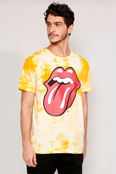 Modelo veste camiseta tie dye amareloa com o símbolo da banda Rolling Stones nela: uma boca com a língua pra fora
