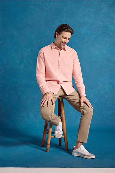 Modelo veste camisa de linho rosa, calça chino bege e tênis branco