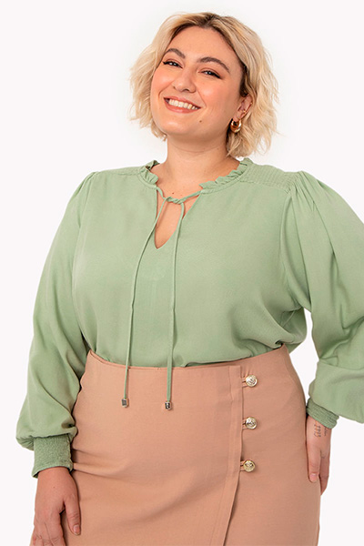 Modelo plus size veste blusa de viscose com amarração no decote e mangas volumosas na cor verde pistache e saia bege