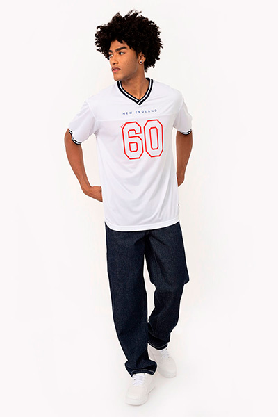 Modelo veste camiseta de time verde branca com o número 60 escrito em vermelho vazado na parte da frente e calça jeans wide leg escura