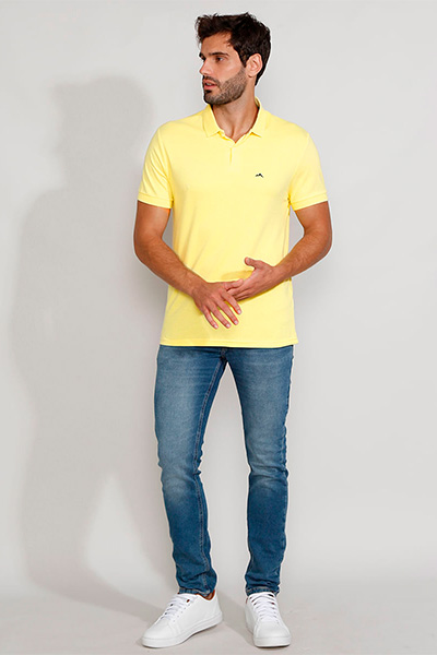 Modelo veste polo amarela, calça jeans de lavagem tradicional e tênis branco