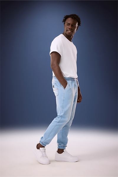 Modelo veste camiseta branca, calça jeans jogger azul e tênis branco
