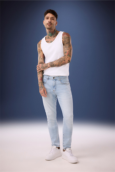 Modelo veste calça jeans slim masculina de lavagem azul clara e regata branca