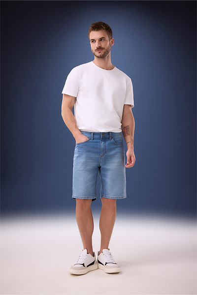 Modelo veste bermuda jeans ampla com lavagem azul clara e camiseta branca