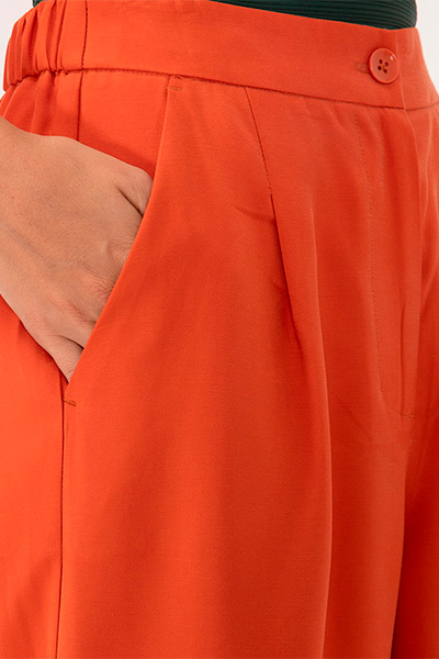 Modelo veste calça wide leg de viscose laranja, chemise da mesma cor e material e top sem alça verde escuro por baixo
