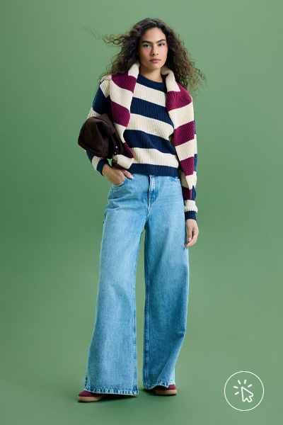 Modelo veste suéter de tricô listrado azul marinho e branco, outro suéter listrado vinho e branco colocado sobre os ombros e calça jeans wide leg