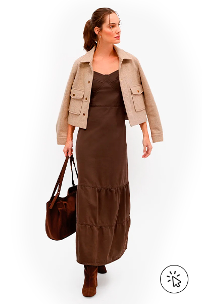 Na foto, a modelo está usando um vestido marrom, uma jaqueta bege, uma bolsa e uma bota marrom - o que dar de presente de dia das mães - o que comprar para o dia das mães - roupa para o dia das mães