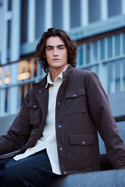 Modelo veste camisa masculina branca e jaqueta parka marrom com bolsos utilitários. Peças fazem parte da coleção de inverno 2025 C&A