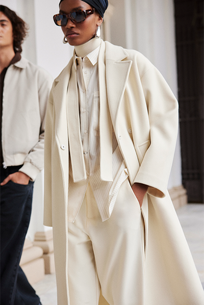 Modelo veste blusa de tricô com gola alta, camisa feminina social, trench coat e calça de alfaiataria, tudo na cor off-white. Peças fazem parte da coleção de inverno 2025 C&A