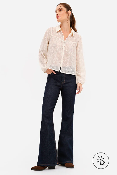 Modelo veste camisa de renda off-white, calça jeans flare cintura alta azul e botas pretas