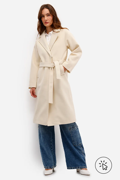 Modelo veste trench coat off-white com faixa, calça jeans cargo e scarpin