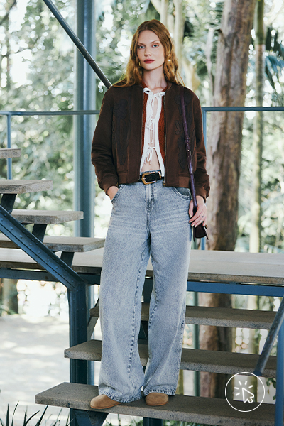 Modelo veste blusa de tricô com amarração frontal terracota, jaqueta marrom e calça jeans oversized lavagem clara