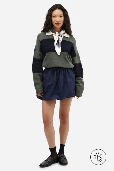 Modelo veste polo manga longa listrada azul marinho e verde musgo, minissaia balonê feminina com cós de elástico azul marinho e mocassim de PU preto com meias pretas