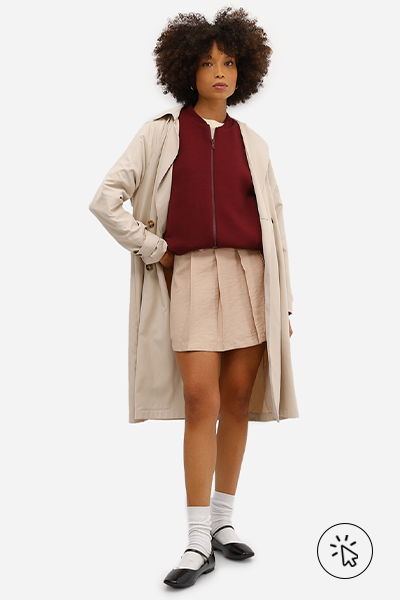 Modelo veste trench coat bege, jaqueta bomber vinho, minissaia feminina de viscose com pregas bege e sapatilha boneca preta