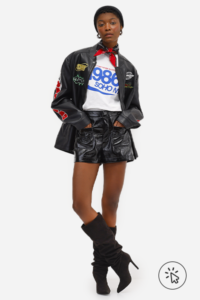 Modelo veste jaqueta biker preta com patches coloridos, camiseta branca com estampa azul 1986, short feminino de couro PU da collab C&A + Stylists assinado por Daniel Ueda e botas over the knee de suede pretas