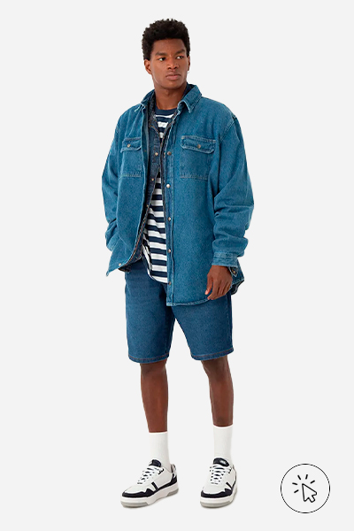 Modelo veste camiseta oversized masculina listrada, bermuda reta masculina jeans azul e jaqueta jeans no mesmo tom