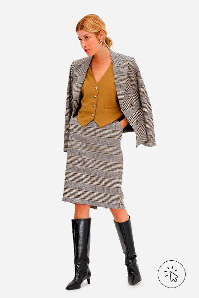 Modelo veste colete feminino de alfaiataria em viscose bege, blazer pied de poule cinza e saia mídi na mesma padronagem e cor, com botas over the knee pretas