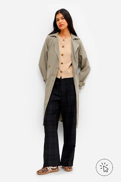 Modelo veste colete feminino de tricô bege, trench coat verde oliva por cima e calça wide leg preta