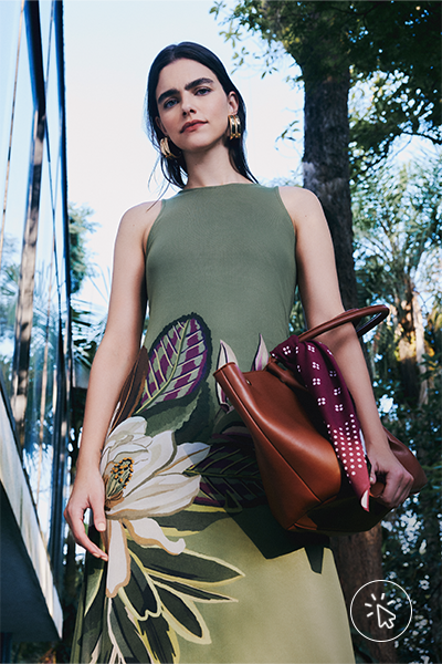 Modelo veste vestido mídi sem mangas com estampa tropical verde pastel e bolsa shopper caramelo com lenço vinho amarrado nela