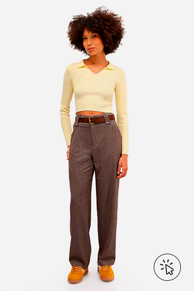 Modelo veste polo básica feminina de tricô manga longa amarelo manteiga e calça de alfaiataria marrom