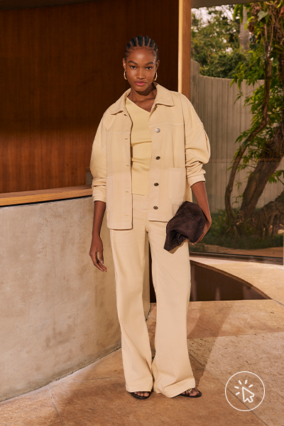 Modelo veste jaqueta oversized de sarja amarelo manteiga, blusa de um ombro só e calça wide leg, tudo na mesma cor