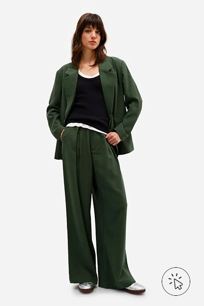 Modelo veste calça de alfaiataria feminina em viscose de modelagem ampla e blazer oversized, ambos verde escuro