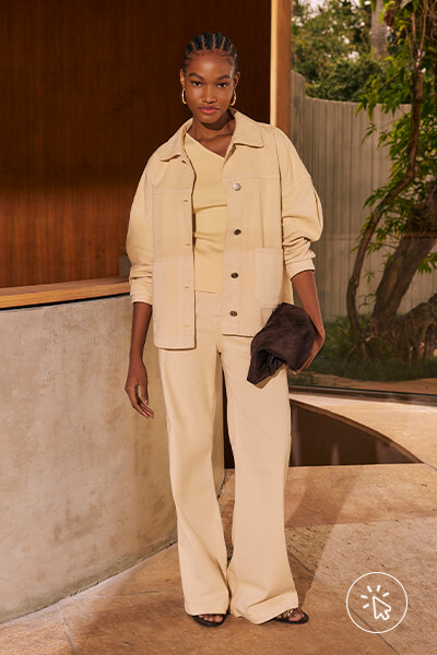Modelo veste jaqueta oversized de sarja amarelo manteiga, blusa de um ombro só e calça wide leg, tudo na mesma cor