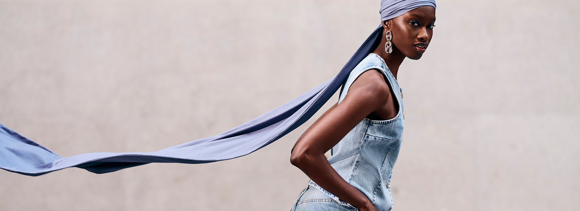 A foto é uma modelo em movimento, andando pra frente, e o lenço jeans que ela está usando está voando atrás dela.