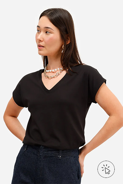 Modelo veste blusa feminina de algodão peruano com decote v preta, wide leg jeans cintura alta azul e mix de brincos e colares de perolas com detalhes dourados - tecidos que não desbotam