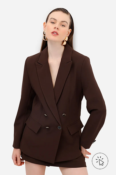 Modelo veste blazer marrom alongado de abotoamento duplo, maxi brincos dourados e short-saia marrom - roupas anos 80 - look anos 80 - moda anos 80 - como era a moda nos anos 80