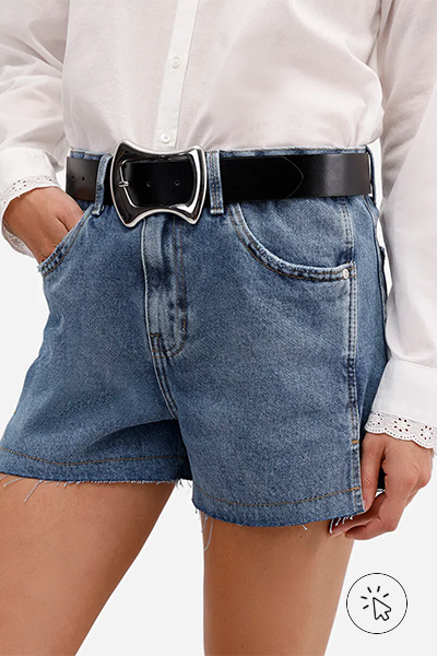 Modelo veste camisa off-white, short jeans azul e cinto preto largo com fivela prateada em formato geométrico - roupas anos 80 - look anos 80 - moda anos 80 - como era a moda nos anos 80