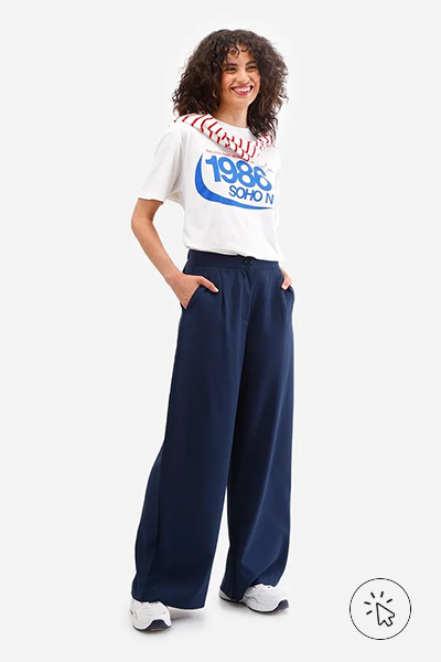 Modelo veste camiseta branca estampada, calça wide leg azul-marinho, tênis branco e suéter listrado vermelho usado sobre os ombros - roupas anos 80 - look anos 80 - moda anos 80 - como era a moda nos anos 80