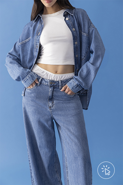 Modelo veste camisa jeans oversized sobre cropped branco ajustado, combinando com calça jeans de modelagem ampla e cintura alta - história do jeans - como surgiu o jeans - como é feito o tecido jeans - tipos de jeans tecido - modelagens de jeans 