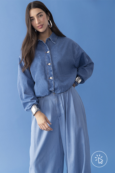 Modelo veste jaqueta jeans cropped com modelagem balonê, calça jeans estilo aladim em tecido maleável, brincos alongados prateados e braceletes prateados sobre os punhos da jaqueta - história do jeans - como surgiu o jeans - como é feito o tecido jeans - tipos de jeans tecido - modelagens de jeans  - história do jeans - como surgiu o jeans - como é feito o tecido jeans - tipos de jeans tecido - modelagens de jeans 