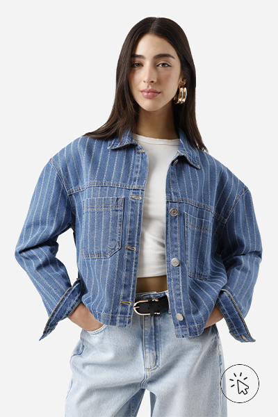 Modelo veste jaqueta jeans cropped com listras verticais e bolsos frontais, cropped off-white, calça jeans de lavagem clara, cinto preto e maxi argolas douradas - história do jeans - como surgiu o jeans - como é feito o tecido jeans - tipos de jeans tecido - modelagens de jeans 