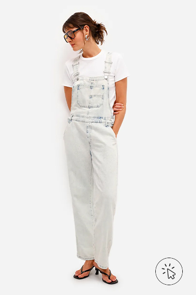Modelo veste jardineira jeans de lavagem clara com modelagem reta, camiseta off-white básica, tamanco preto e óculos escuros - história do jeans - como surgiu o jeans - como é feito o tecido jeans - tipos de jeans tecido - modelagens de jeans 