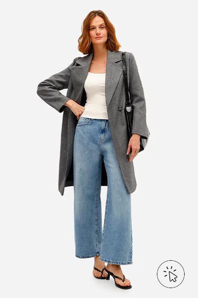 Modelo veste trench coat cinza, regata off-white, calça jeans de modelagem ampla, tamanco preto e bolsa tote preta - história do jeans - como surgiu o jeans - como é feito o tecido jeans - tipos de jeans tecido - modelagens de jeans 