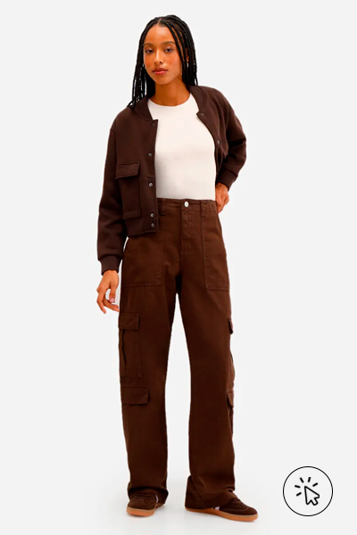 Modelo veste calça cargo feminina de sarja cintura média marrom, jaqueta no mesmo material e da mesma cor com camiseta básica branca por baixo