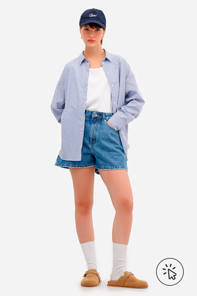 Modelo veste camiseta branca, camisa oversized  azul clara por cima, short feminino jeans cintura alta azul e mule clog bege
