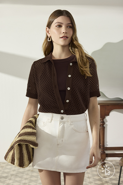 Modelo veste camisa de tricô marrom, camiseta marrom por baixo e minissaia de sarja off-white