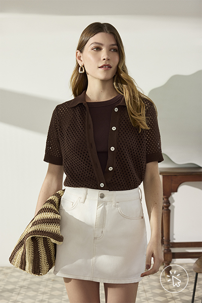 Modelo veste camisa de tricô marrom, camiseta marrom por baixo e minissaia de sarja off-white