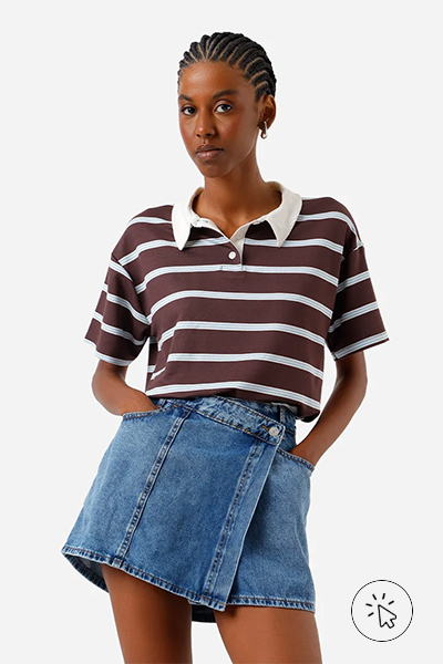 Modelo veste short-saia feminina jeans com cós deslocado azul e polo listrada marrom - cores que combinam com azul