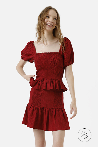 Modelo veste conjunto vermelho escuro de blusa com mangas bufantes e saia curta com babado